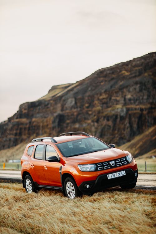 Free Dynamic shot of an orange SUV parked on a rural road beside a towering hill. Stock Photo
