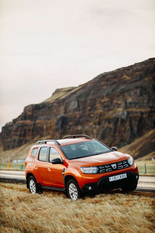 Free Bright orange SUV on a rural road against a rocky mountain backdrop, perfect for adventure travel themes. Stock Photo