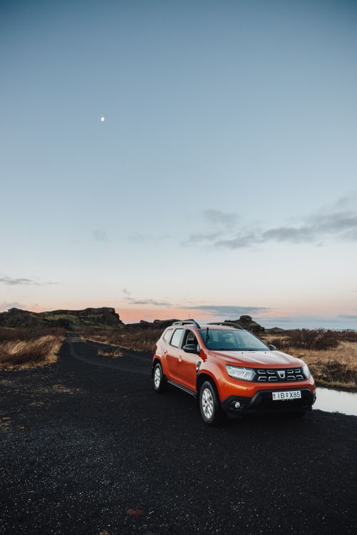 Free Orange SUV parked on a rural dirt road with a clear sky at sunset. Ideal for travel and adventure themes. Stock Photo