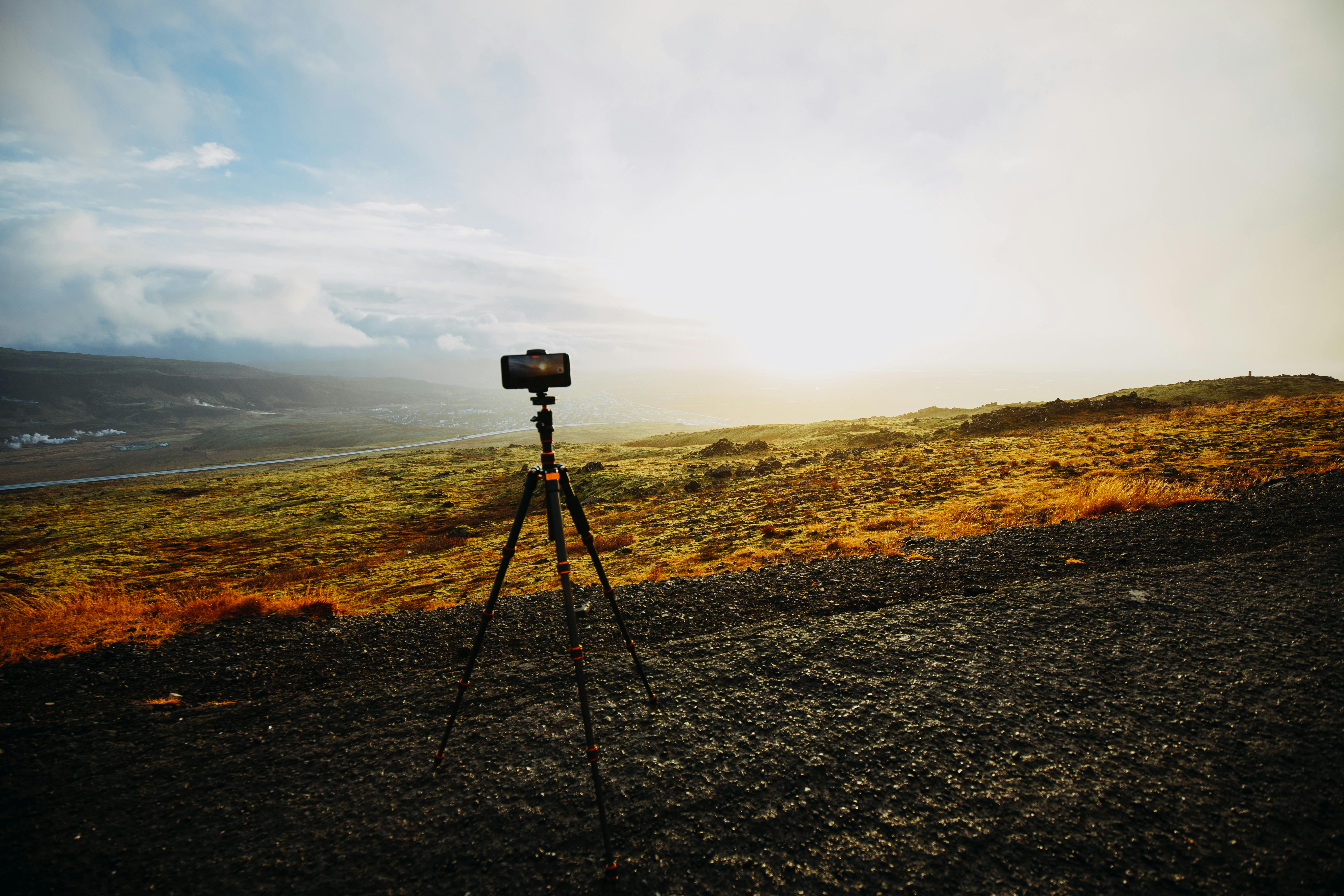 A serene countryside view with a camera on tripod capturing the scenic landscape at sunrise.