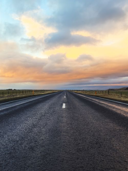Free Enjoy the serene beauty of a solitary road stretching through Iceland's picturesque landscape at sunset. Stock Photo