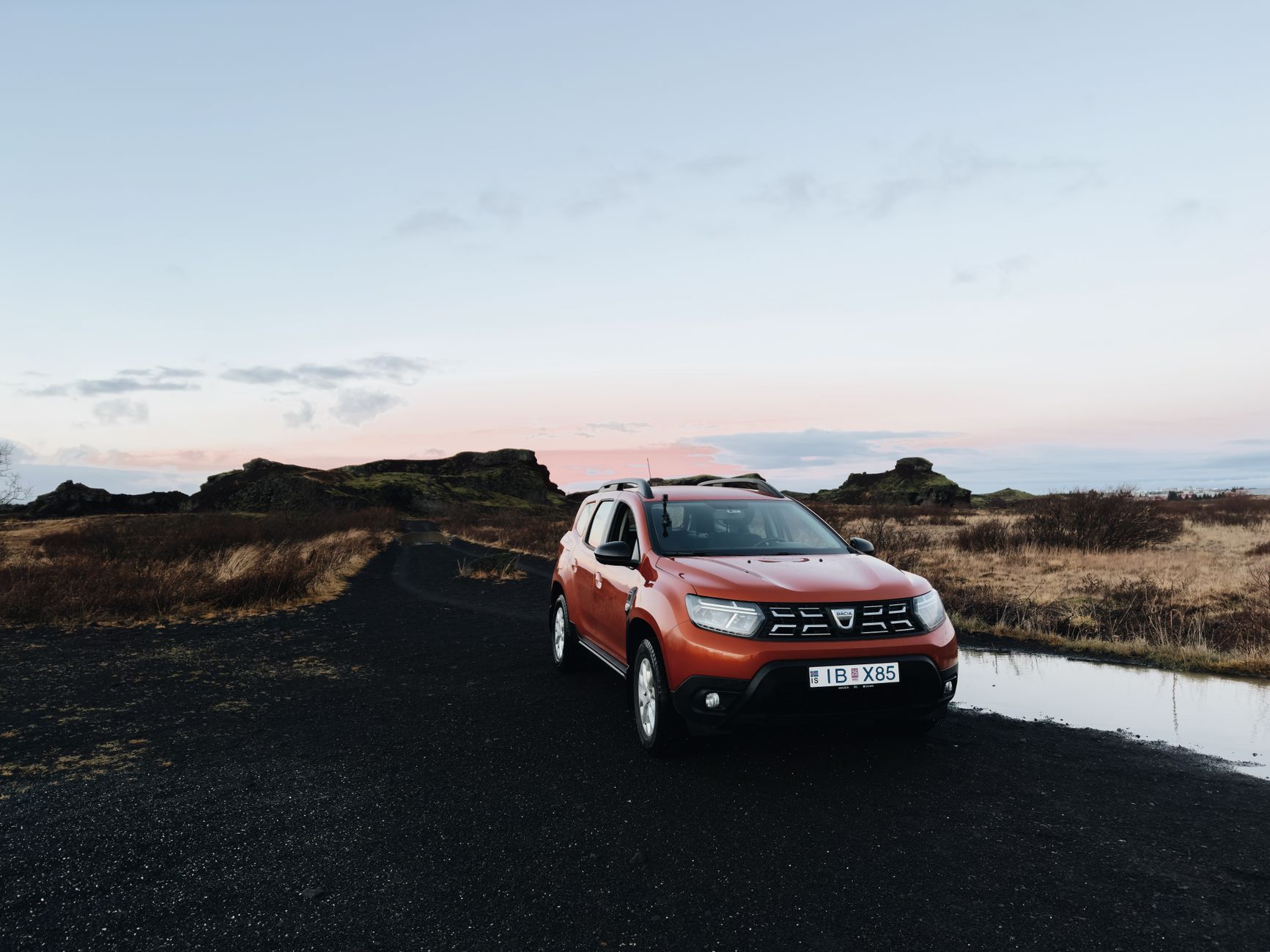 Rental car parked on a gravel pull-off along the Ring Road with mountains behind