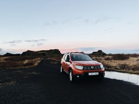 An orange SUV parked on a dirt road in Iceland's countryside at sunset.