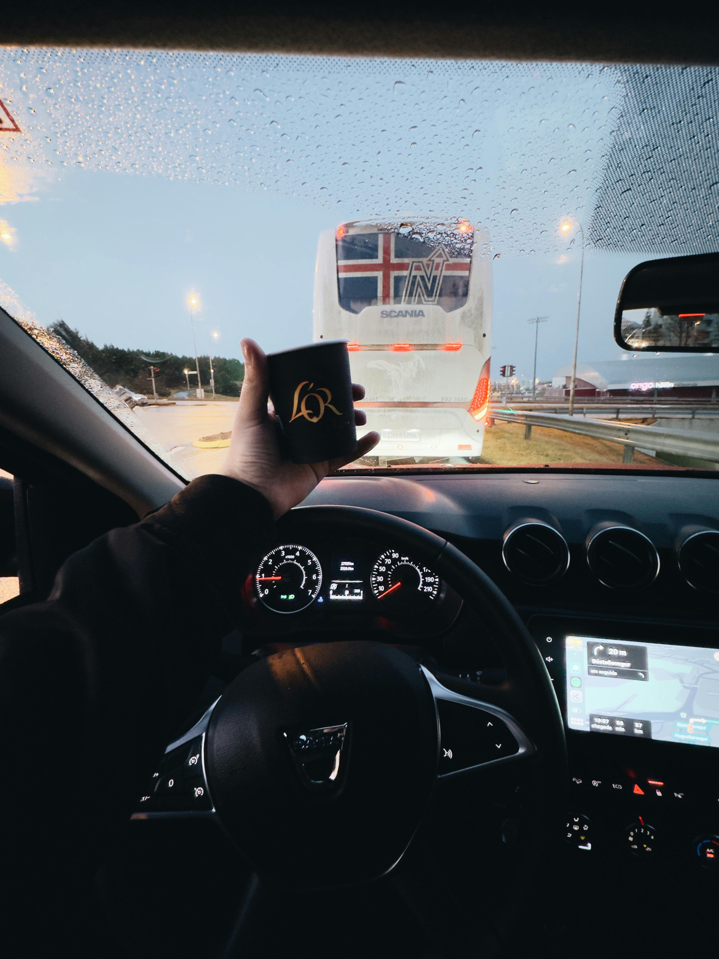 Driving in Reykjavík, Iceland, holding a coffee cup with a view of the road and a bus ahead.