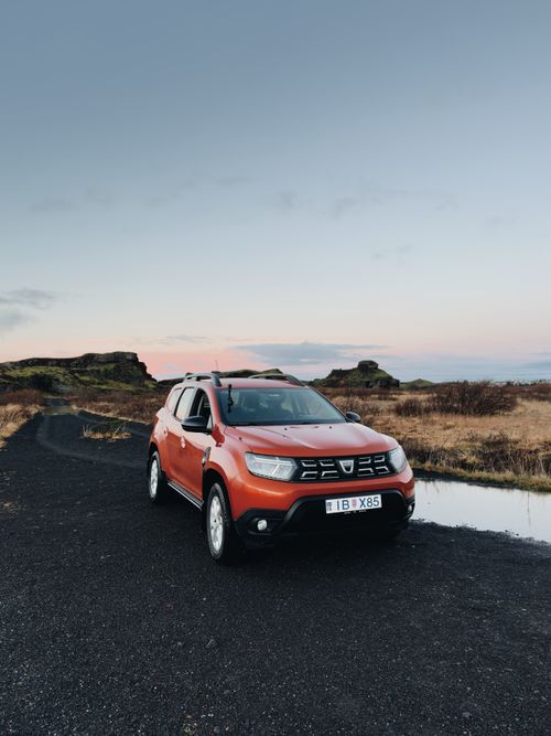 Free Explore the rugged beauty of Iceland with this bold orange SUV on a scenic dirt road at dusk. Stock Photo