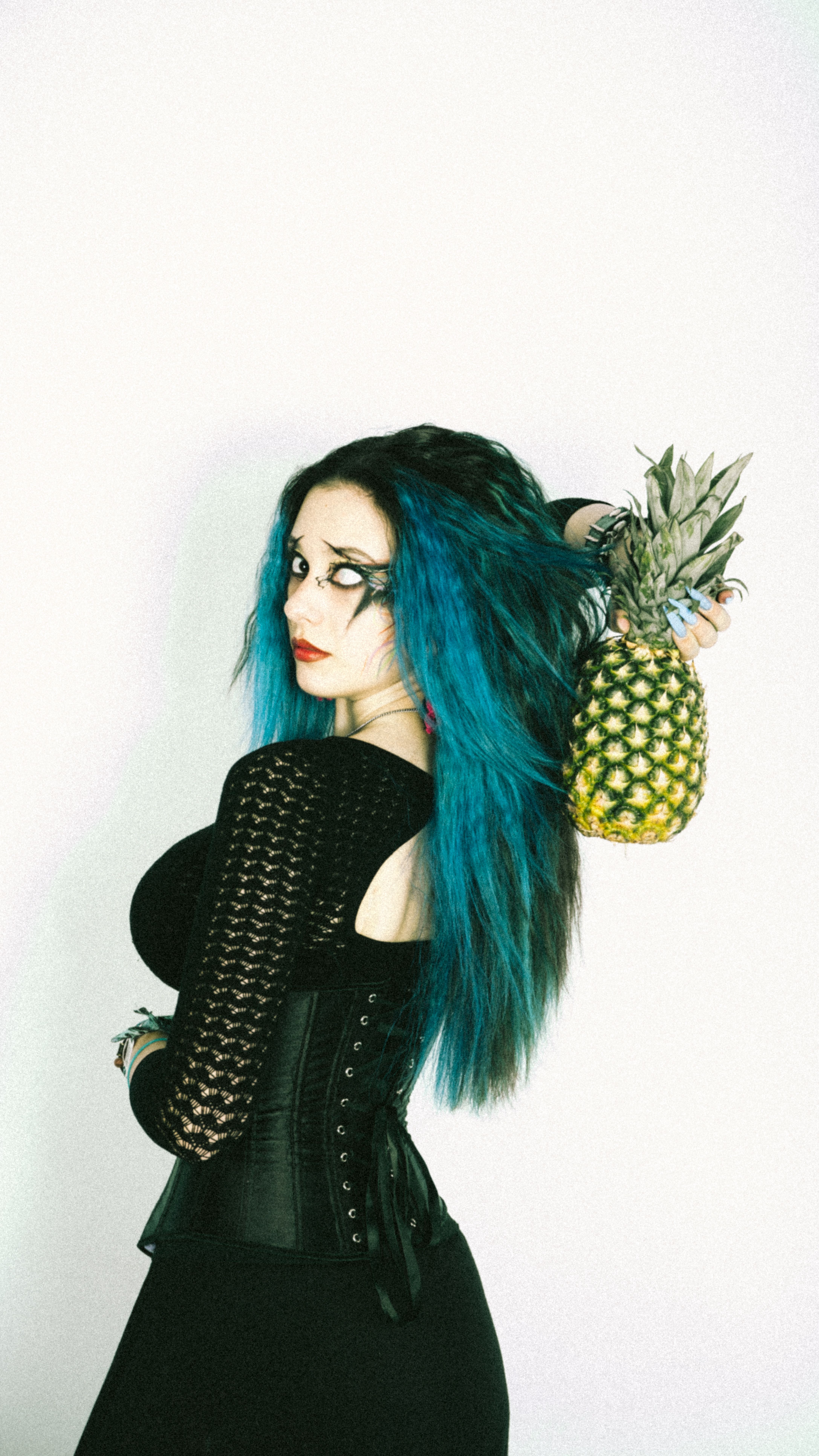 Portrait of a woman with vibrant blue hair holding a pineapple, showcasing gothic fashion style.