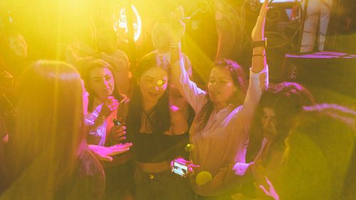 Free Group of friends enjoying a lively night out at a club with vibrant yellow lighting and music. Stock Photo