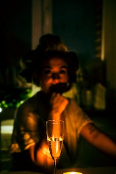 A woman sitting at night with a champagne glass in focus, creating a moody atmosphere.