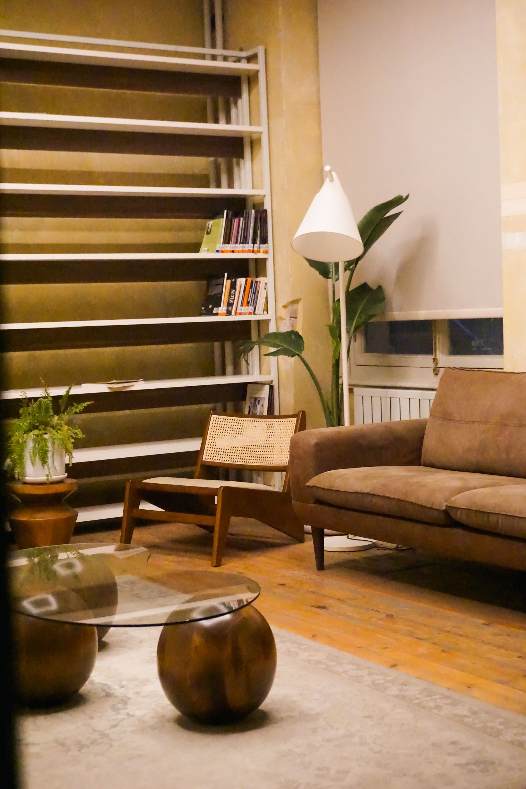 Brown living room with a leather-look sofa, timber floor, wood-and-cane chair, bronze-toned table and pale walls
