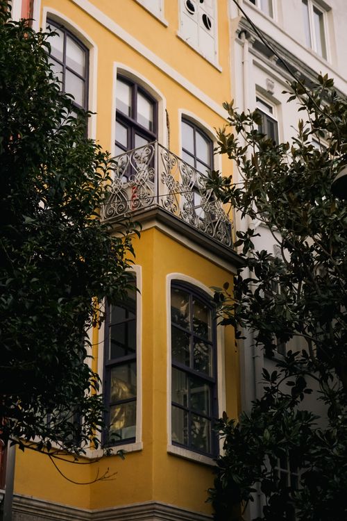 Free A stylish yellow building facade with decorative balcony among lush trees. Stock Photo
