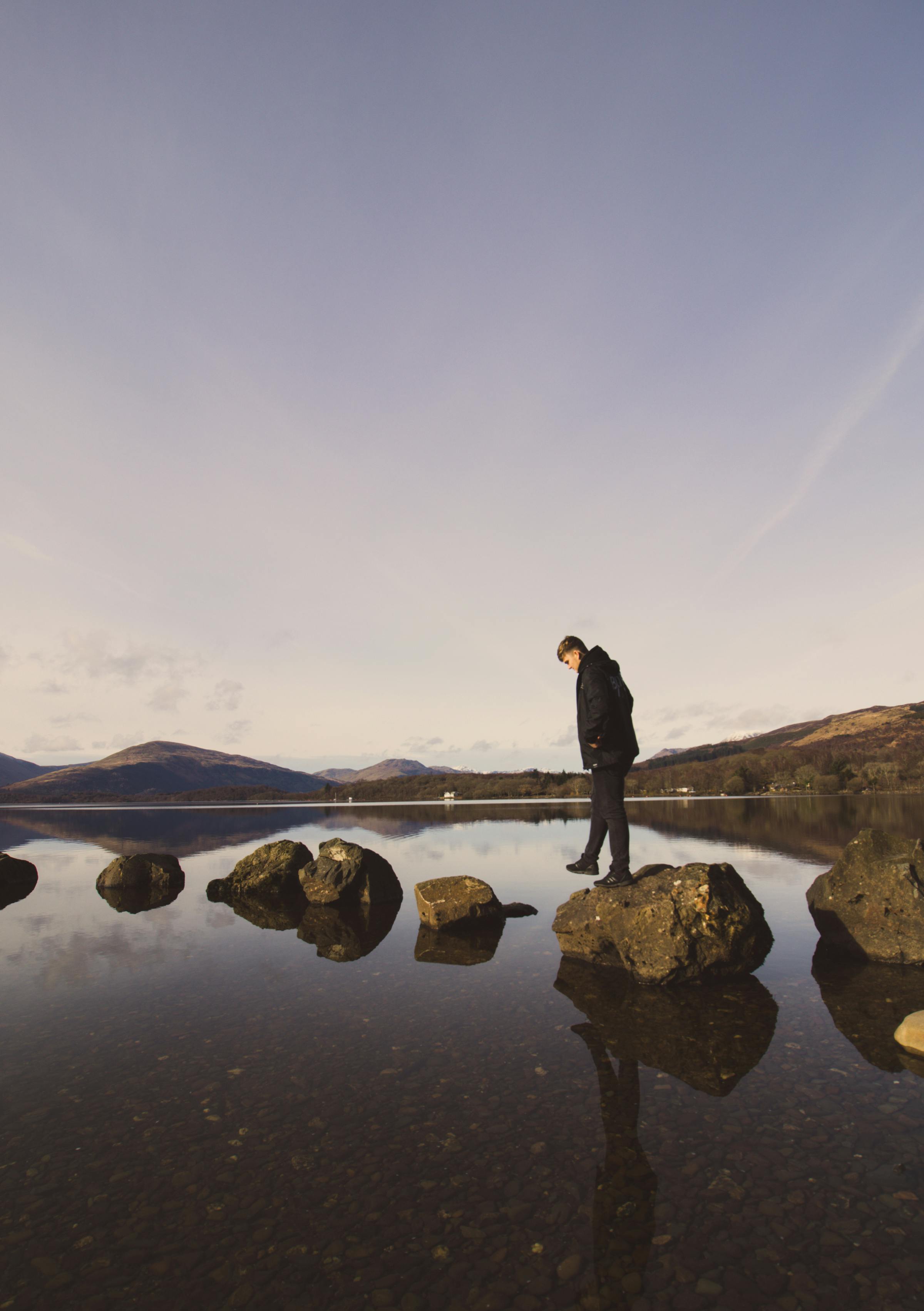 日落时分，一个人站在平静湖泊的岩石岸边，四周环绕着宁静的大自然