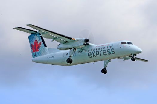 Air Canada Express plane soaring through the sky with a maple leaf design on a cloudy day.