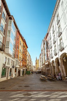 Explore a picturesque alley in Burgos, Spain, with vibrant buildings under a clear sky.