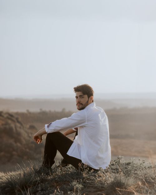 Free A thoughtful adult man sitting on a hilltop in a white shirt, enjoying the serene landscape. Stock Photo