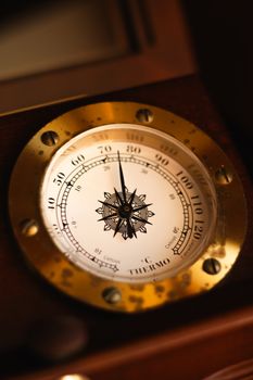 Close-up of a vintage brass thermometer with a nautical compass design, capturing precise temperature details.