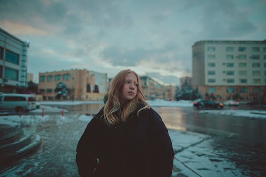 Young woman in black jacket stands outdoors in snowy Baku, Azerbaijan, during winter.