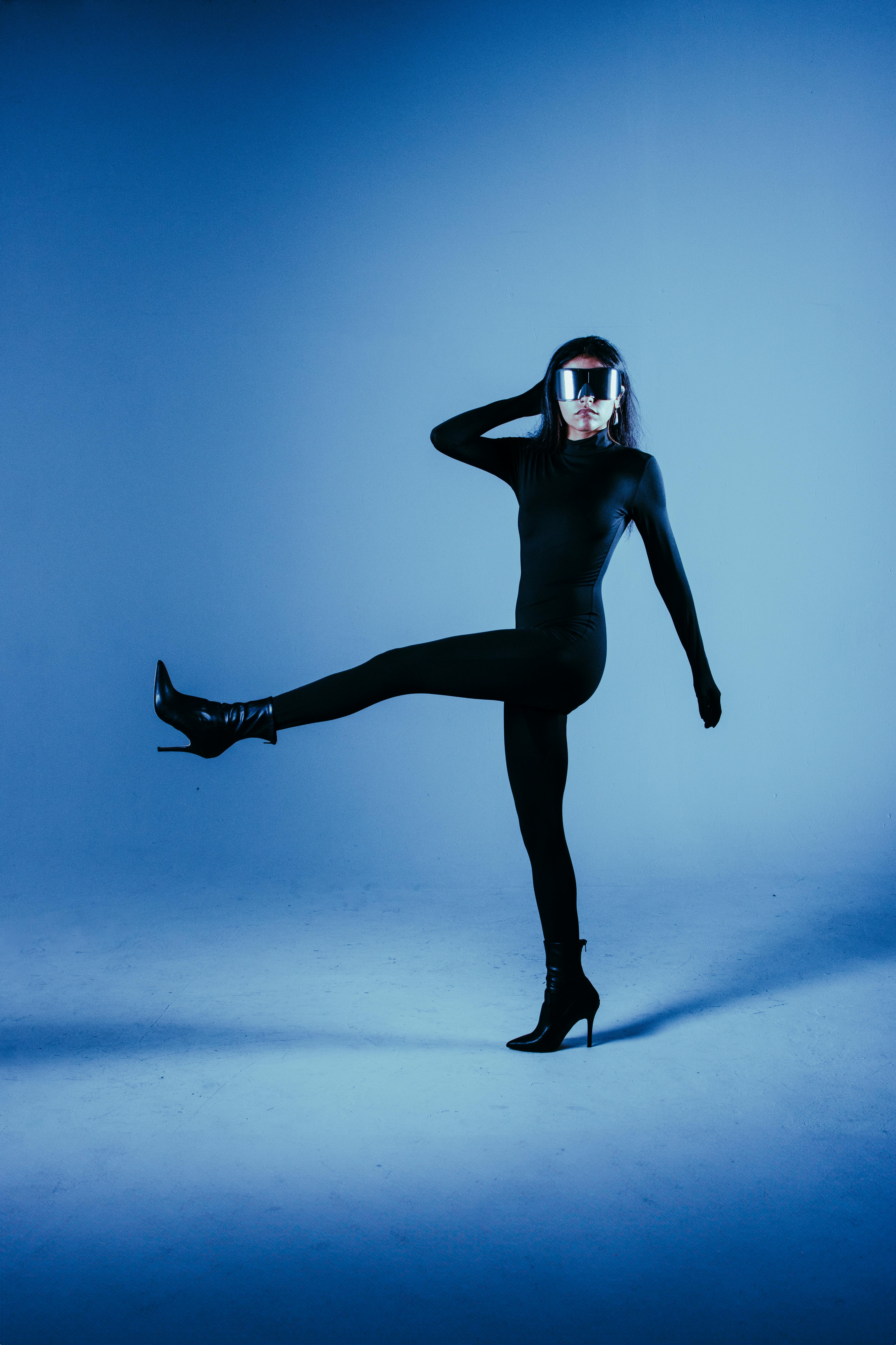 A modern portrait of a woman in a sleek black outfit with eyewear, exuding futuristic vibes under blue lighting.