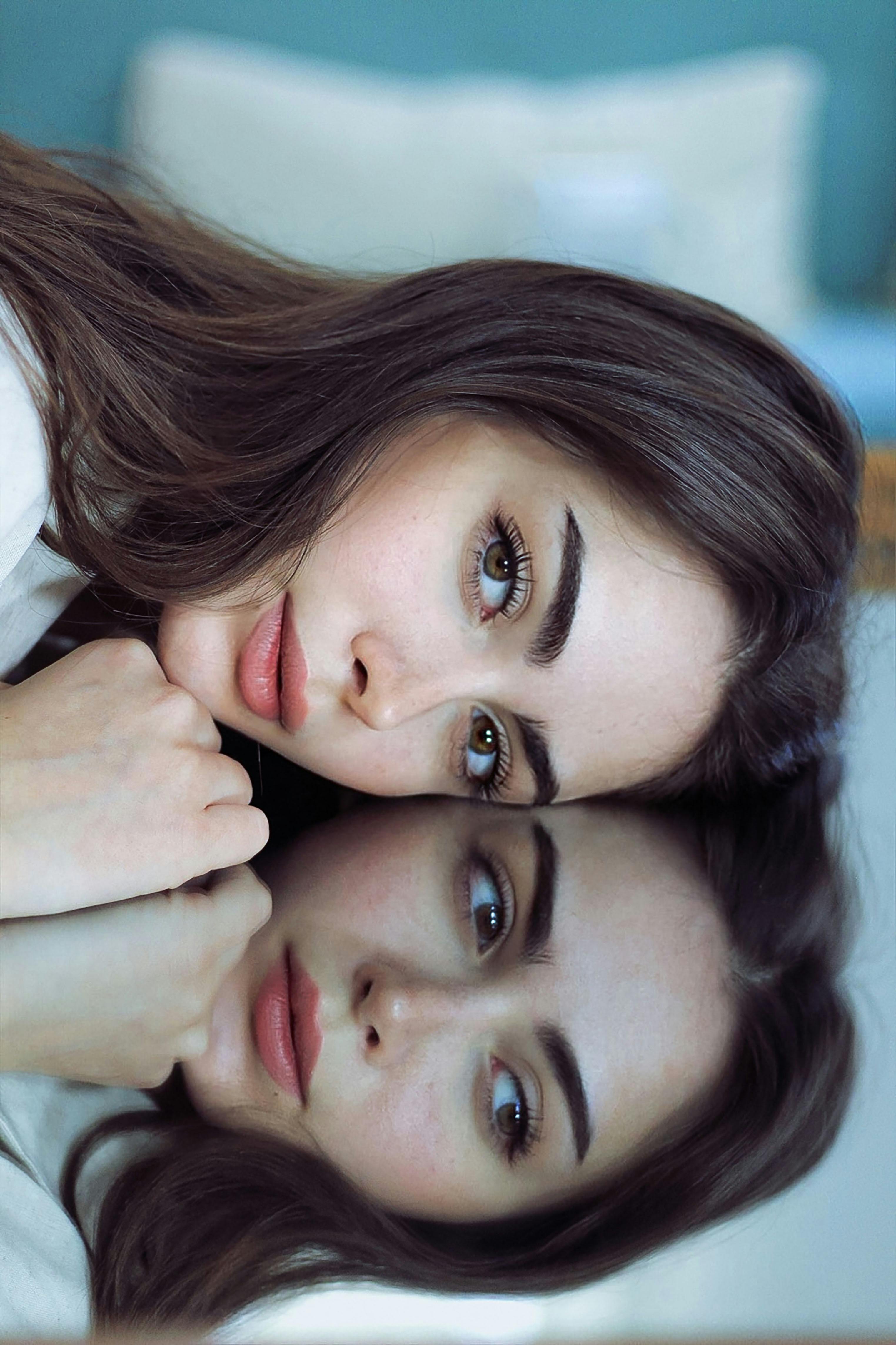 Stunning portrait of a woman with long brown hair reflecting in a mirror, showcasing beauty and elegance.