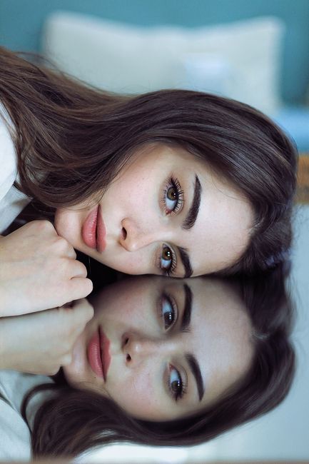 Stunning portrait of a woman with long brown hair reflecting in a mirror, showcasing beauty and elegance.
