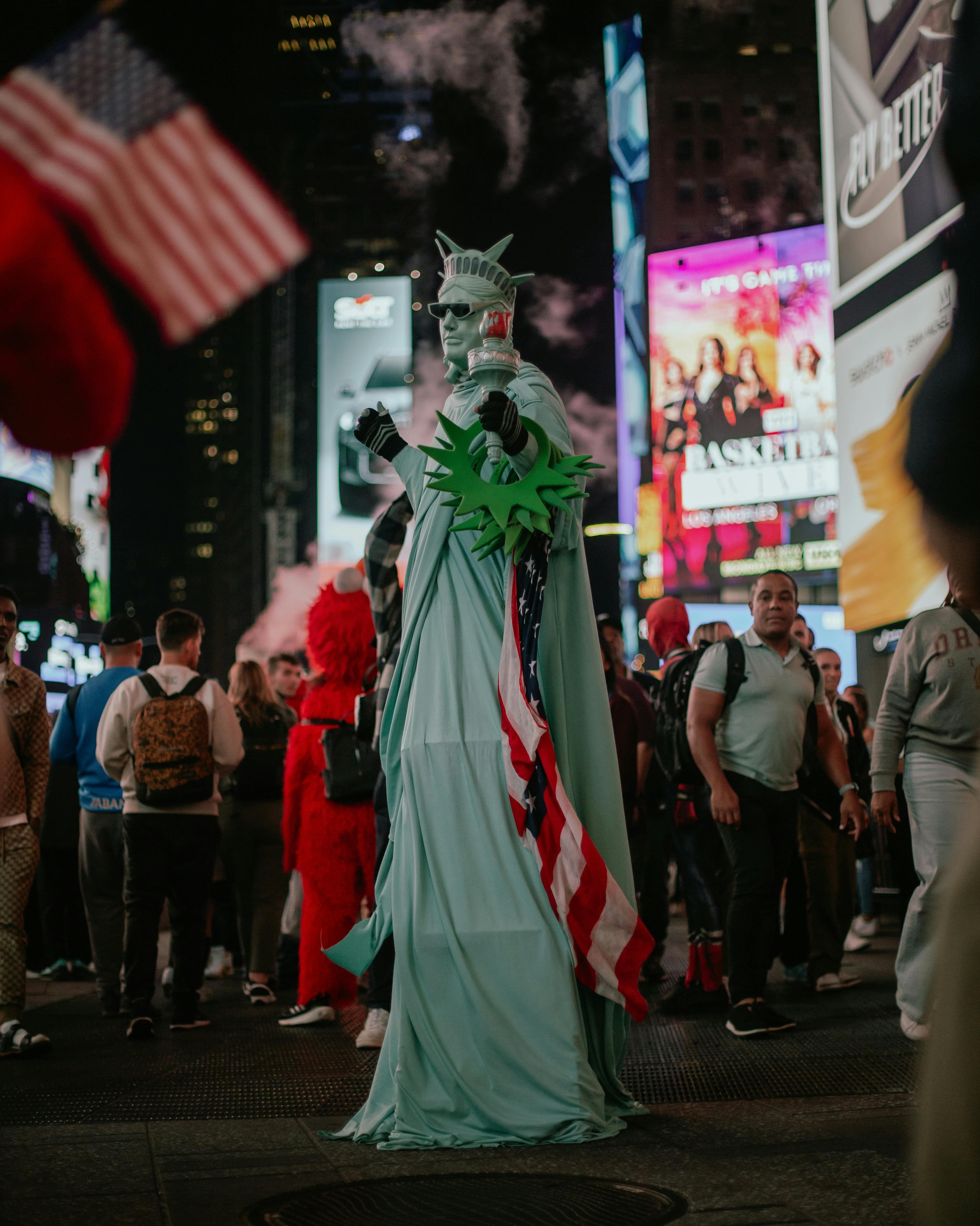 Street performer dressed as the Statue of Liberty in vibrant Times Square with American flag.