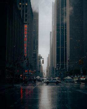 Moody street scene featuring Radio City Music Hall in New York City during a rainy evening.