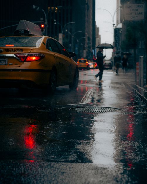 Free Rain-soaked streets of New York City featuring a yellow taxi and pedestrians with umbrellas. Stock Photo