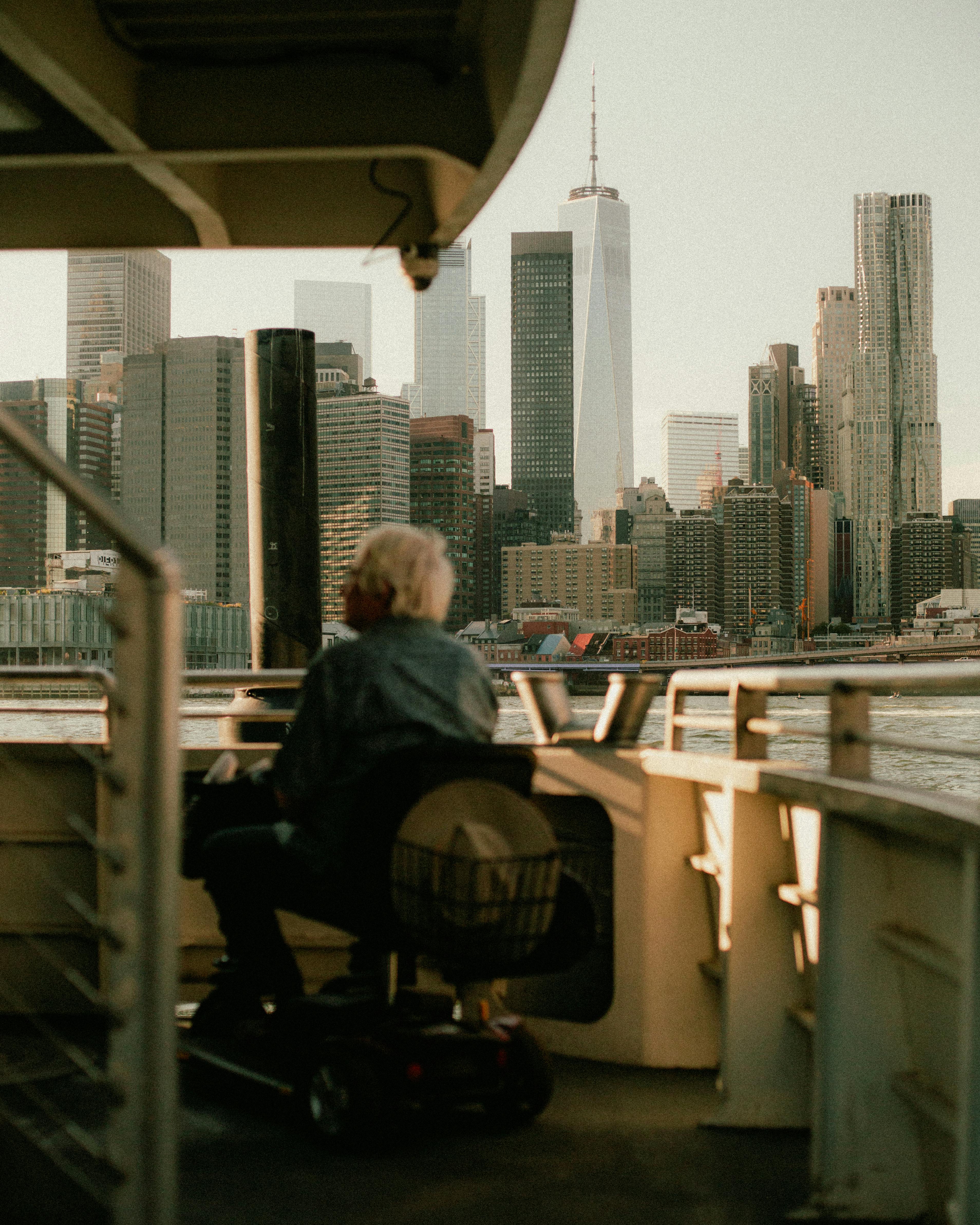 Elderly person on ferry viewing New York City skyline, featuring iconic skyscrapers.