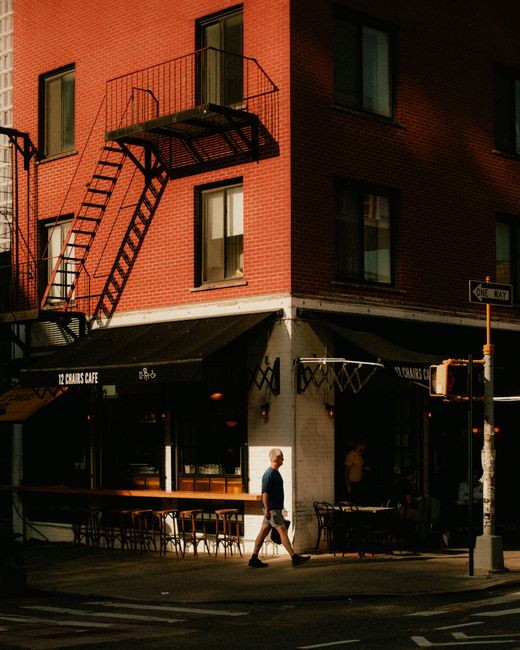 A man walks past a corner cafe in a city street, capturing urban life and architecture.