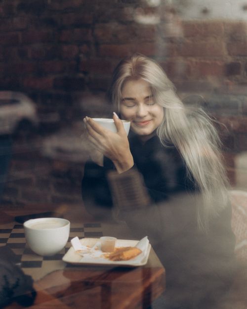 Free Woman enjoying coffee at a cozy café with a serene expression. Warm, inviting atmosphere. Stock Photo