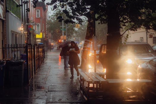 Atmospheric street scene in New York during an evening rain shower, with people walking and bright streetlights.