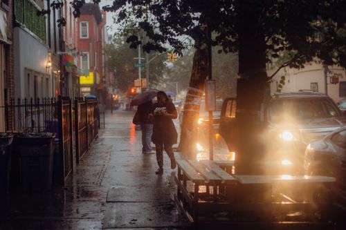 Free Atmospheric street scene in New York during an evening rain shower, with people walking and bright streetlights. Stock Photo
