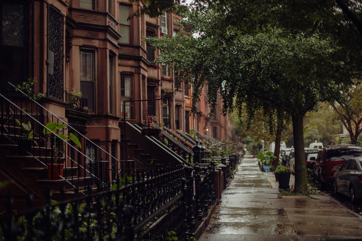 Brownstone homes along a quiet New York street on a rainy day.