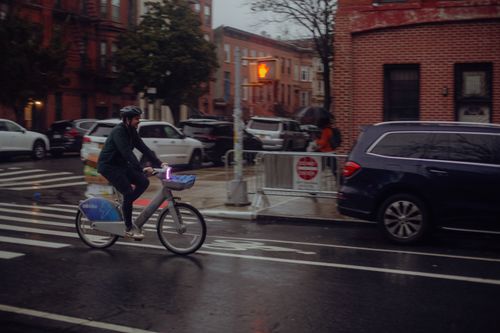 Free Adult male cyclist braving the rain on New York City streets, riding a Citi Bike with urban backdrop. Stock Photo
