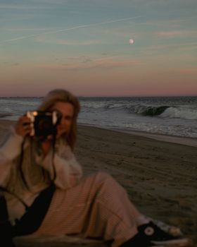 A woman captures the serene twilight on a beach, emphasizing the tranquil atmosphere.