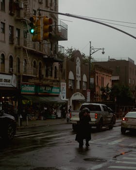 Woman navigating wet city streets under traffic lights on a rainy day.