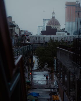 Moody image of a train passing through a rainy New York City street, capturing urban atmosphere.