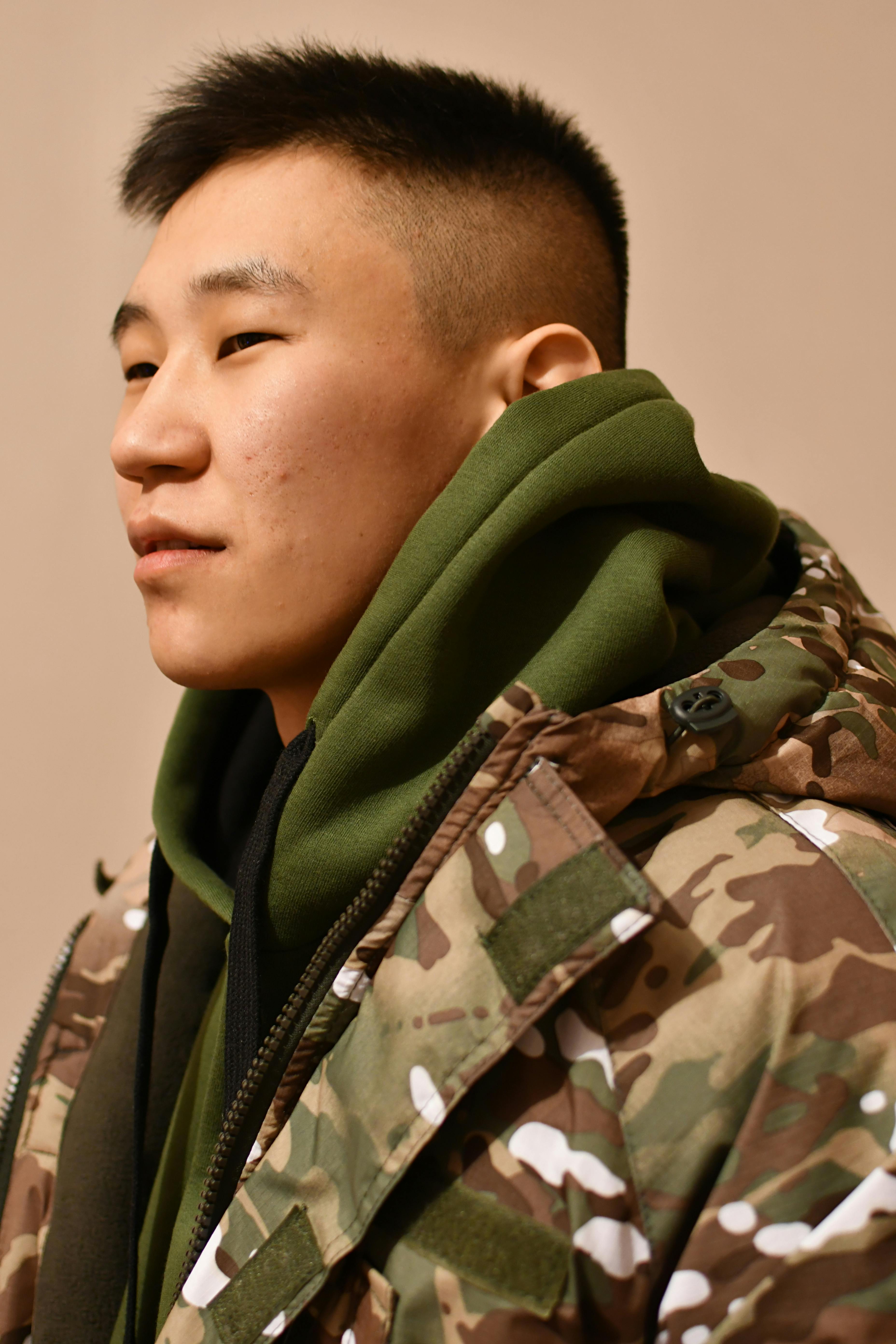 Profile portrait of a man in a stylish camouflage jacket with a green hoodie.