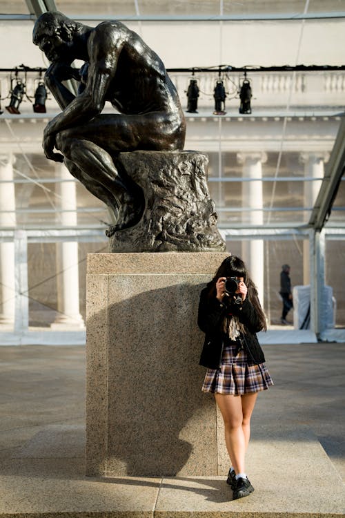 Woman with a Camera Standing next to The Thinker Statue in the California Palace of the Legion of Honor in San Francisco 