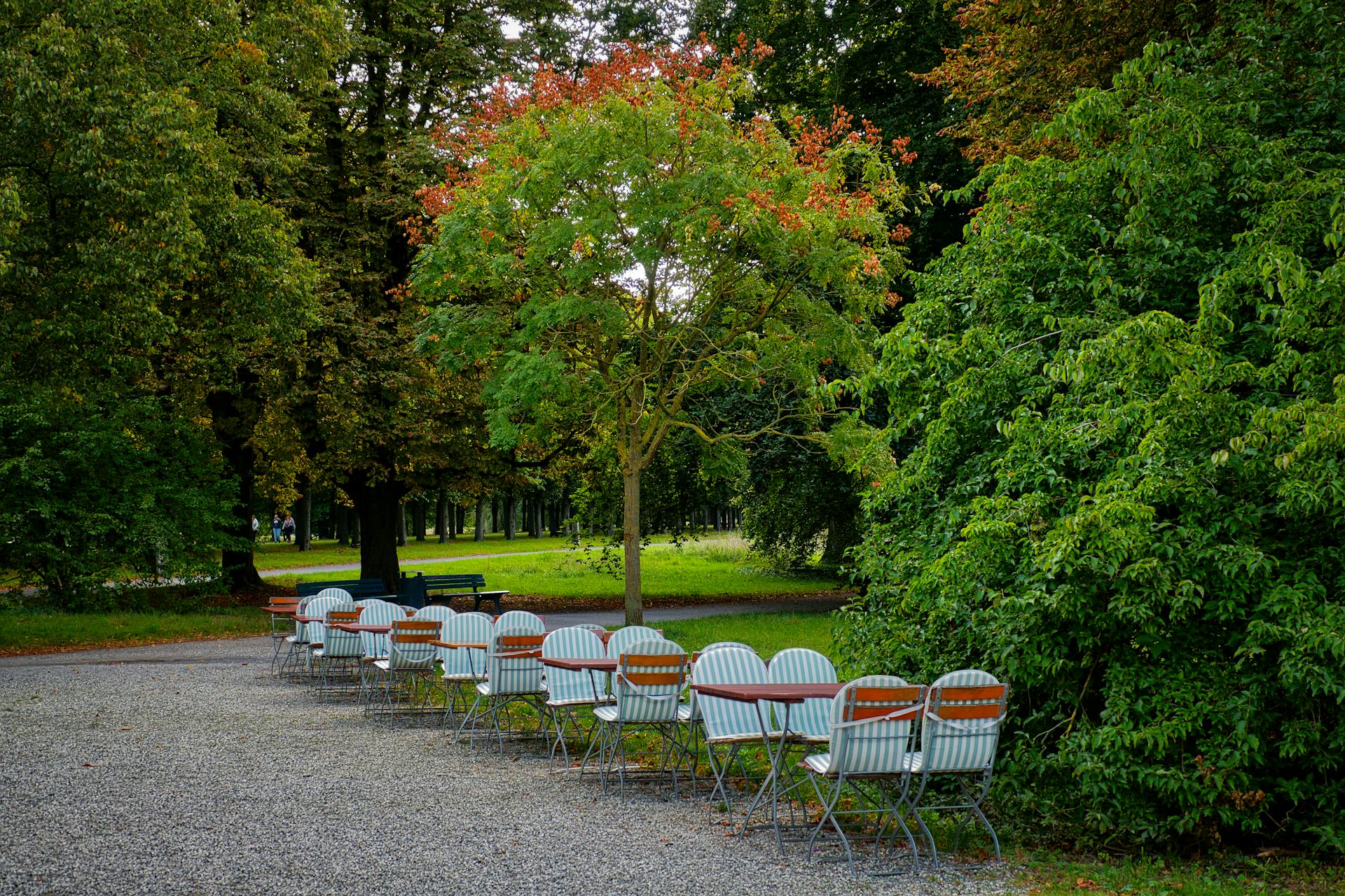 Outdoor café tables and chairs in a lush green Hannover park, perfect for a tranquil retreat.