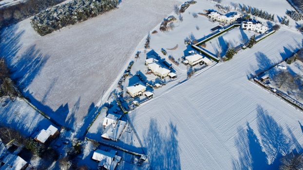 Aerial view of Grez-Doiceau, Belgium covered in snow, featuring fields, trees, and houses.
