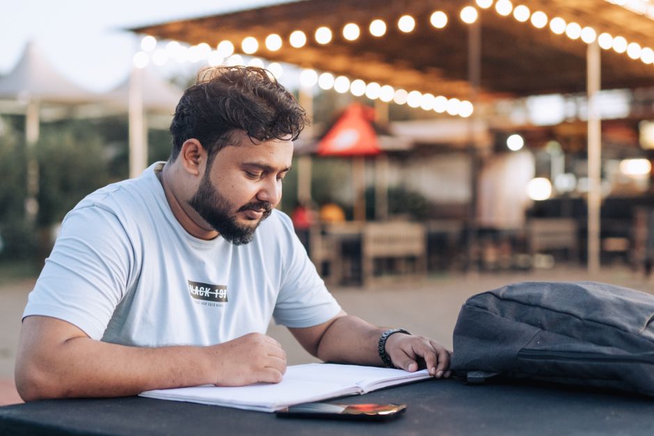 Man studying at an outdoor cafe table with a notebook and backpack in the evening. Man studying at an outdoor cafe table with a notebook and backpack in the evening.