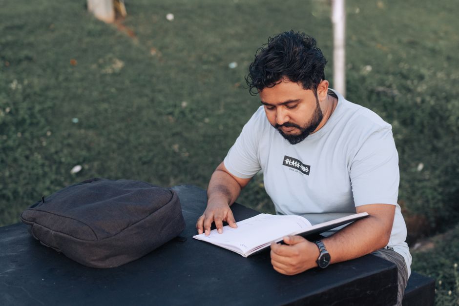 A man with a beard reading a notebook outdoors on a sunny day, wearing a t-shirt. A man with a beard reading a notebook outdoors on a sunny day, wearing a t-shirt.