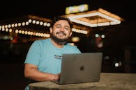 A Bearded Man Sitting at a Table with a Laptop and Smiling