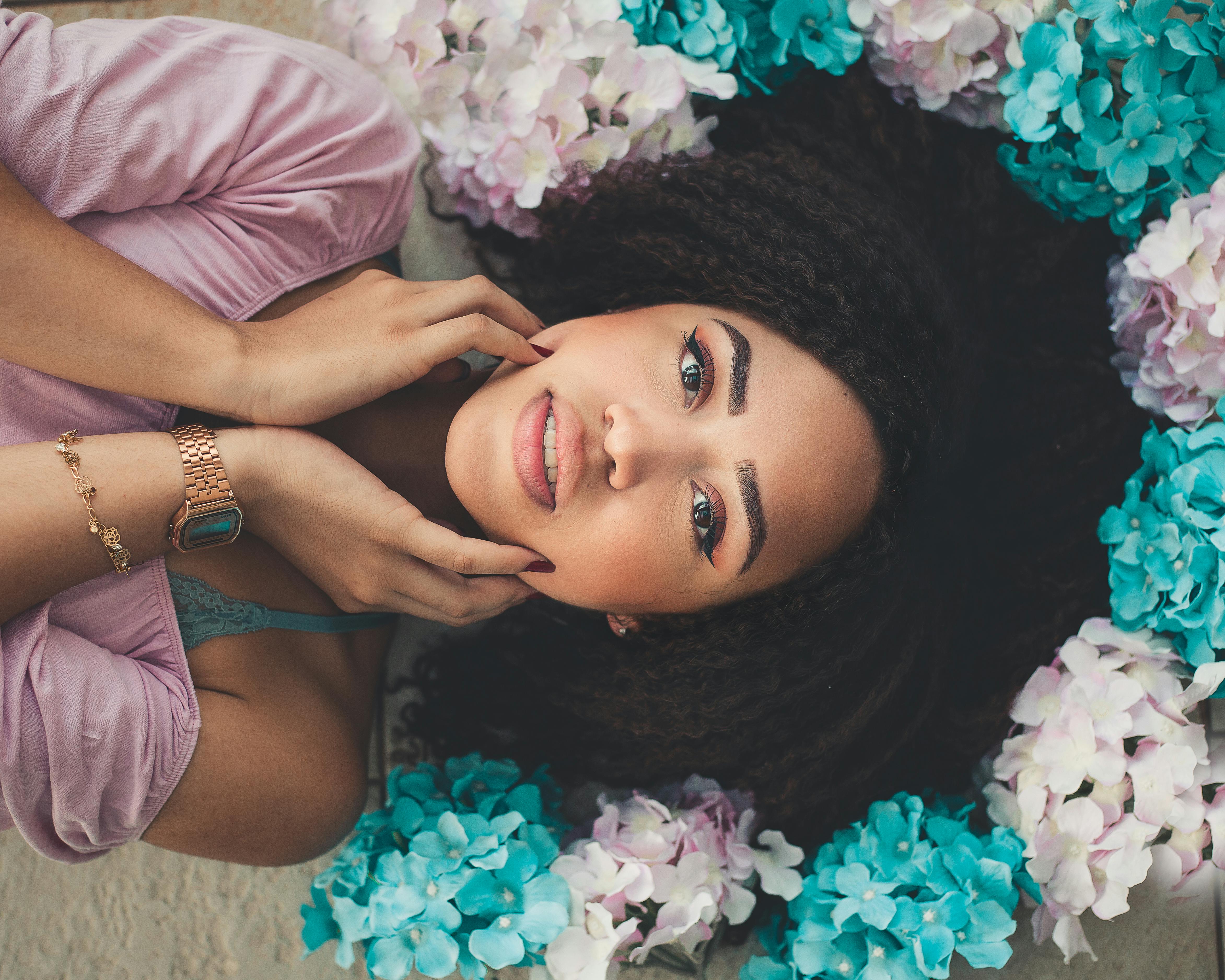 woman lying on white surface with white and teal paper flower around her head