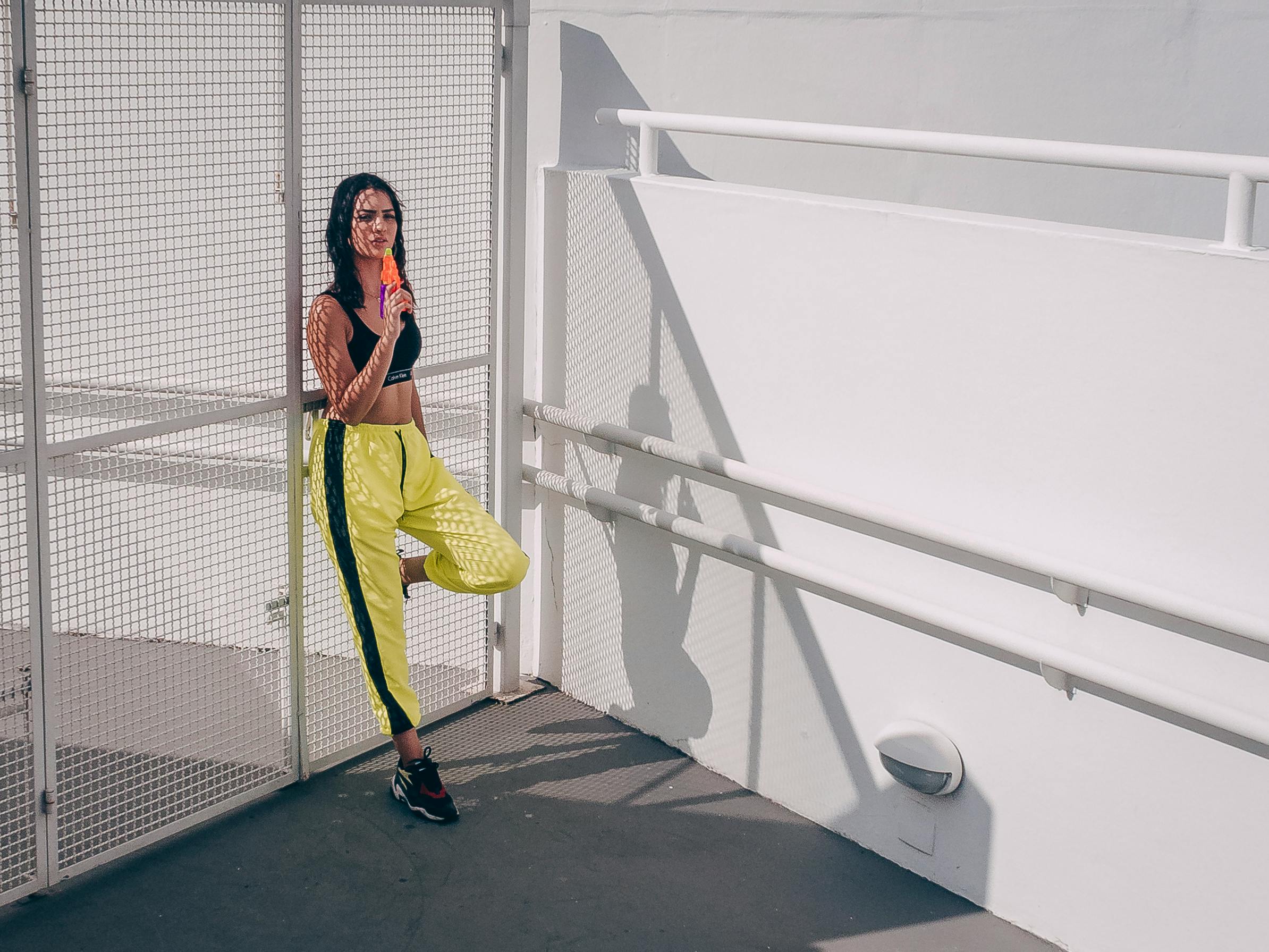 Fashionable woman in workout attire enjoying an ice cream outdoors against a minimalist white background.