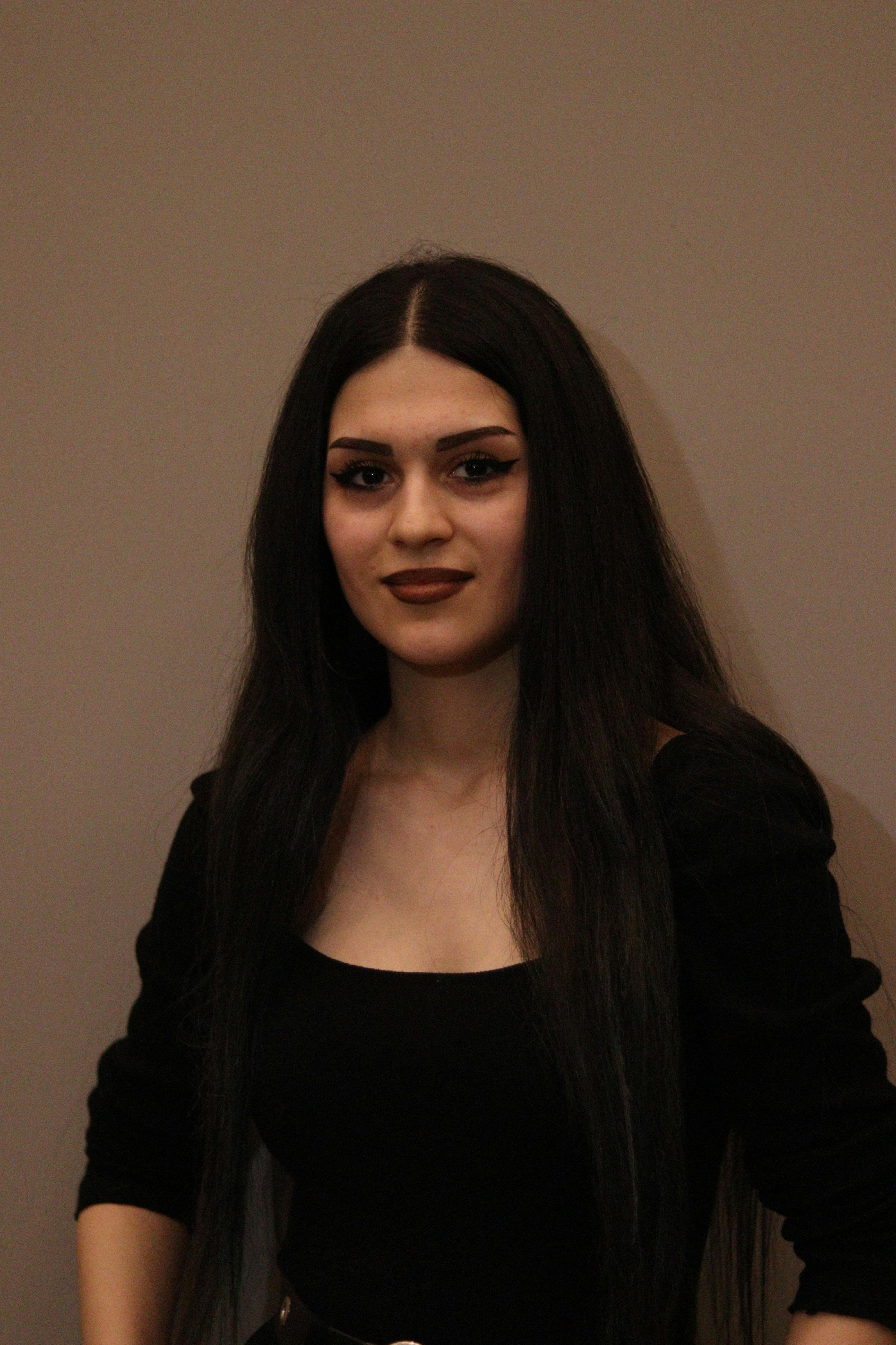 Stylish portrait of a woman with dark hair and bold makeup in a black outfit.