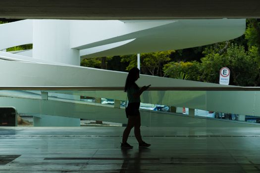 Woman's silhouette walking inside a modern architectural space, focused on her phone.