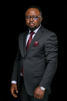 Elegant portrait of a businessman with beard and glasses, wearing a suit against a black background.