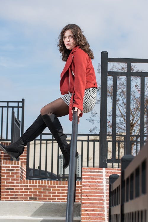 Model in a Red Jacket and a Checkered Mini Skirt Sitting on a Railing