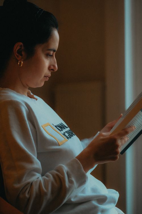 Free A woman with black hair engrossed in a book, sitting indoors with soft lighting. Stock Photo